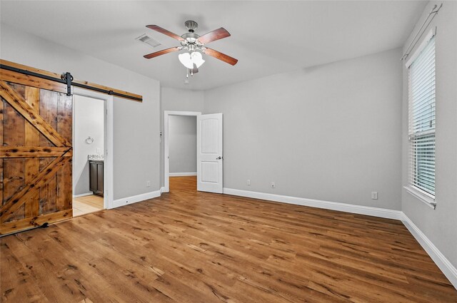 unfurnished bedroom featuring wood finished floors, baseboards, connected bathroom, and ceiling fan