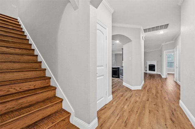 staircase featuring ornamental molding, arched walkways, wood finished floors, baseboards, and a fireplace