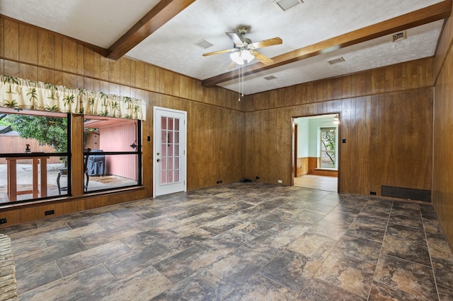spare room with beam ceiling, wood walls, a ceiling fan, stone finish floors, and a textured ceiling