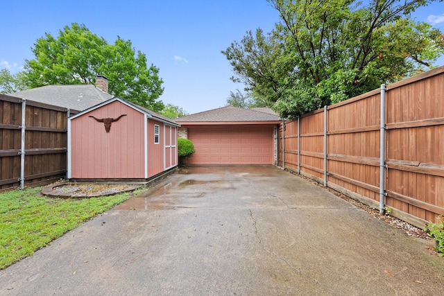 view of vehicle parking with a detached garage, fence, and a storage unit