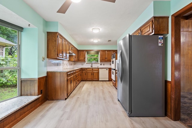 kitchen with white appliances, light wood-style floors, healthy amount of natural light, a sink, and wainscoting