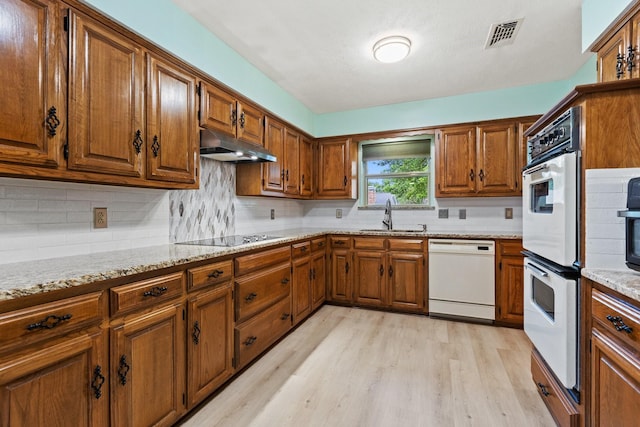 kitchen with white appliances, a sink, under cabinet range hood, and brown cabinets