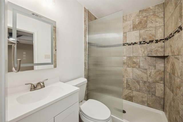 bathroom with toilet, a tile shower, and vanity