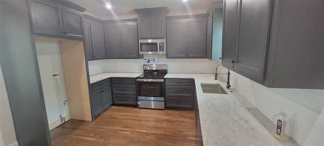 kitchen featuring appliances with stainless steel finishes, a sink, light stone countertops, decorative backsplash, and dark wood-type flooring