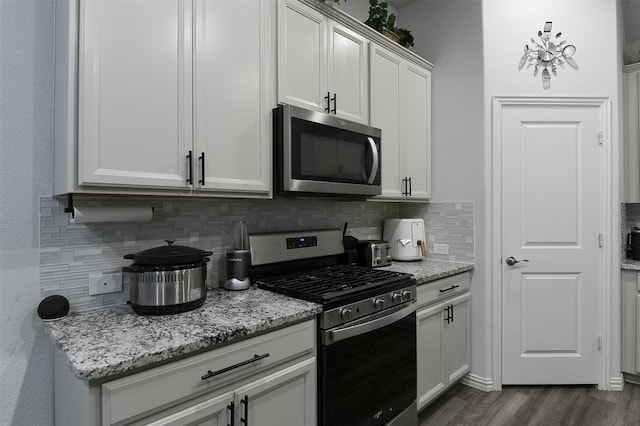 kitchen with appliances with stainless steel finishes, backsplash, dark wood-style flooring, light stone counters, and white cabinetry