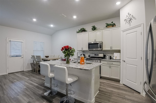 kitchen with appliances with stainless steel finishes, a sink, dark wood-style floors, backsplash, and vaulted ceiling