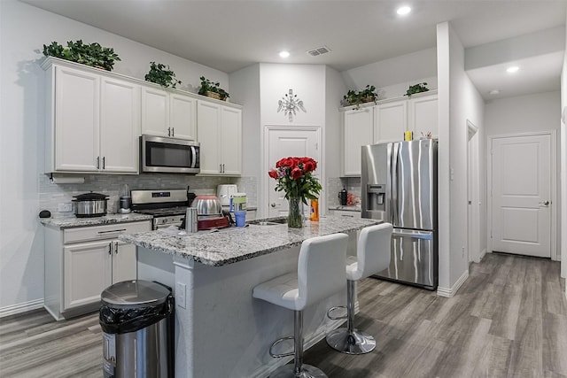 kitchen featuring stainless steel appliances, light wood-type flooring, a kitchen breakfast bar, tasteful backsplash, and recessed lighting
