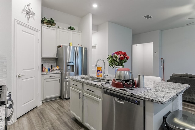 kitchen with a sink, stainless steel appliances, light wood-style floors, an island with sink, and white cabinetry