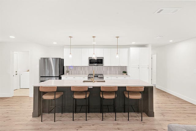 303 Randy Lee Ln, Mckinney, TX 75071 - kitchen featuring appliances with stainless steel finishes, a center island with sink, decorative backsplash, white cabinetry, and light wood-style flooring