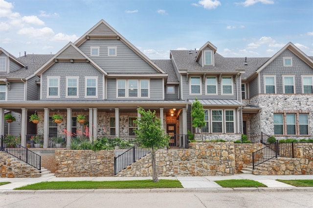 view of front of home with stairway, covered porch, stone siding, and roof with shingles