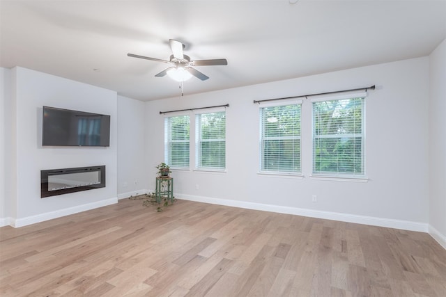 unfurnished living room featuring ceiling fan, light wood-type flooring, a glass covered fireplace, and baseboards