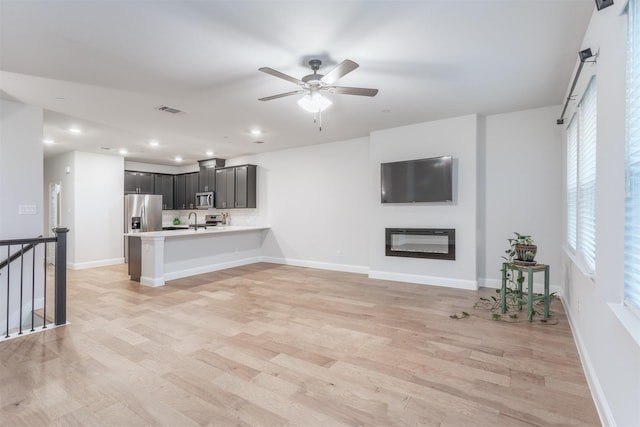 unfurnished living room featuring light wood-style floors, ceiling fan, a sink, recessed lighting, and baseboards