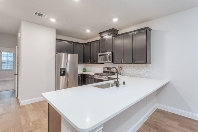 kitchen with stainless steel appliances, a sink, light countertops, baseboards, and tasteful backsplash