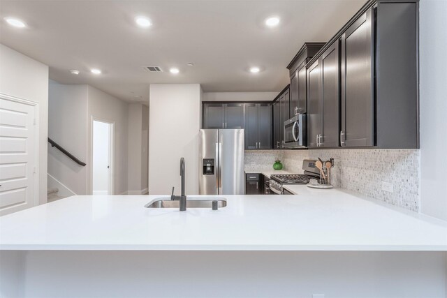 kitchen featuring stainless steel appliances, a sink, recessed lighting, tasteful backsplash, and a peninsula