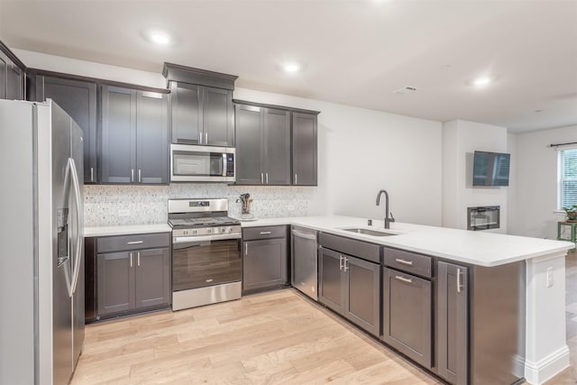 kitchen with stainless steel appliances, a sink, a peninsula, light wood finished floors, and backsplash