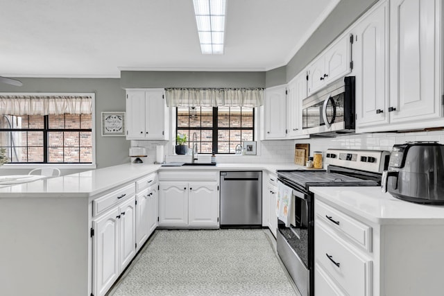 kitchen featuring appliances with stainless steel finishes, a peninsula, crown molding, backsplash, and light countertops