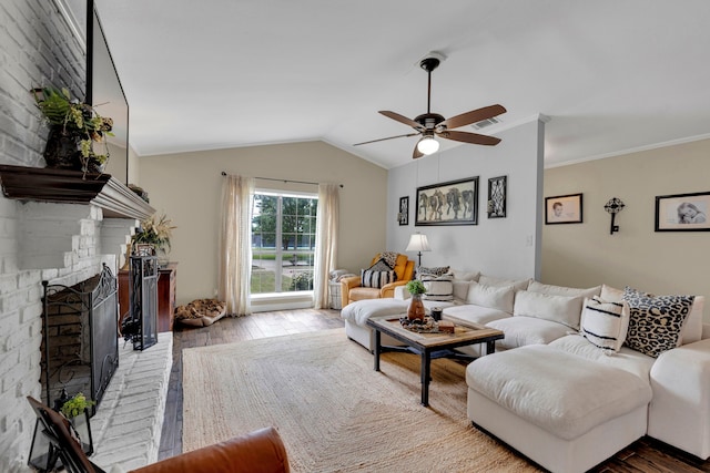 living area featuring wood-type flooring, ceiling fan, vaulted ceiling, a brick fireplace, and crown molding
