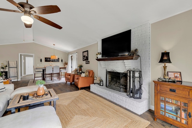 living area with ceiling fan, wood finished floors, a fireplace, lofted ceiling, and ornamental molding