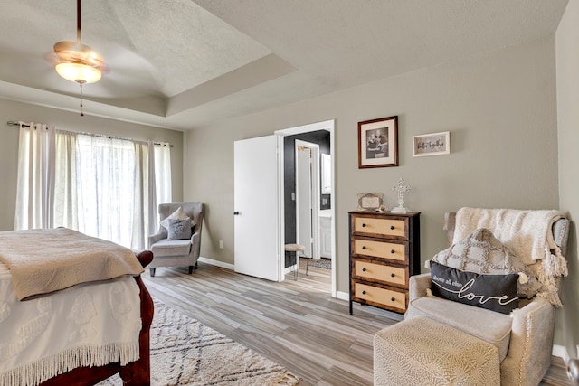 bedroom with a raised ceiling, baseboards, a textured ceiling, light wood-style floors, and ensuite bathroom