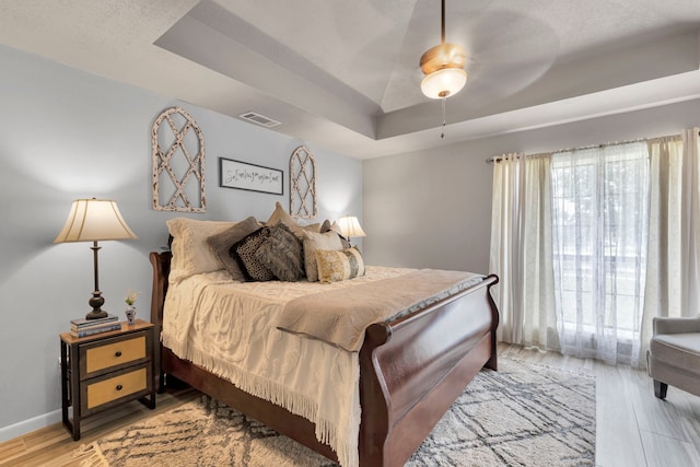 bedroom with a raised ceiling, light wood finished floors, baseboards, and ceiling fan