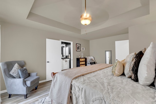 bedroom with a raised ceiling, light wood-type flooring, baseboards, a ceiling fan, and ensuite bathroom