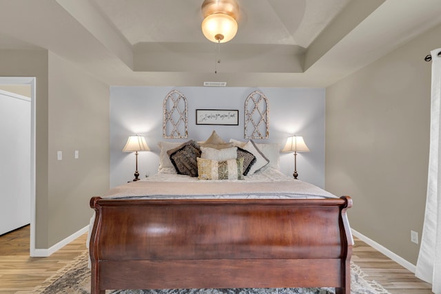 bedroom featuring a raised ceiling, light wood-type flooring, baseboards, and ceiling fan