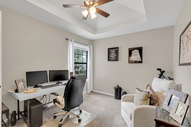 carpeted home office with ceiling fan, baseboards, and a raised ceiling