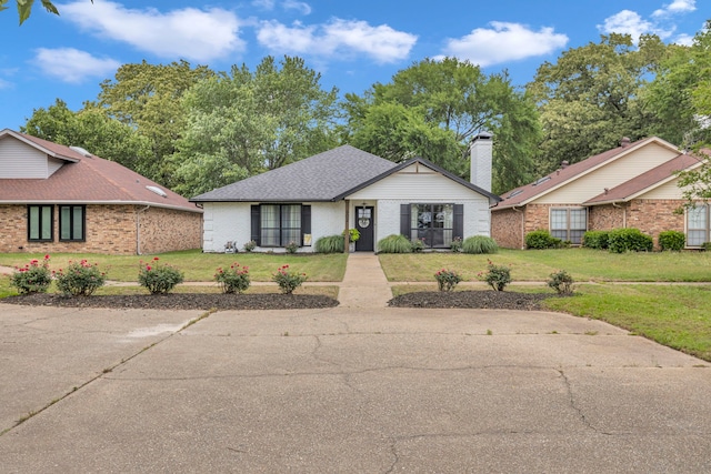 ranch-style home featuring brick siding, a front lawn, and roof with shingles