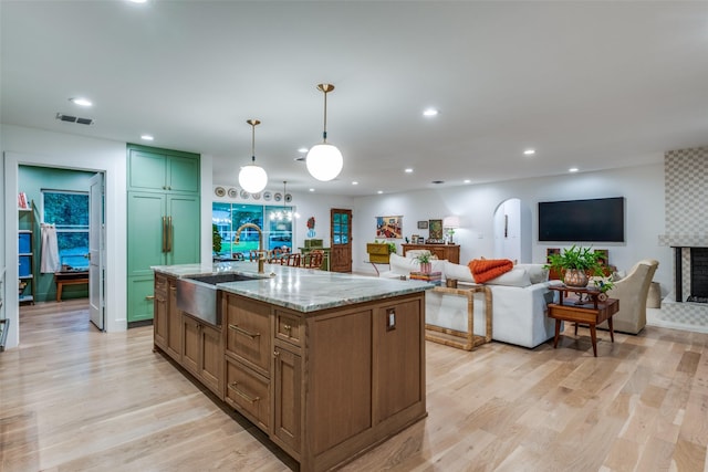 kitchen featuring a sink, light wood-style flooring, light stone counters, recessed lighting, and an island with sink