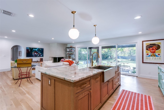 kitchen with a sink, arched walkways, light wood-type flooring, pendant lighting, and recessed lighting