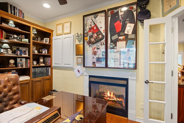 office area featuring crown molding, wood finished floors, a glass covered fireplace, and a ceiling fan