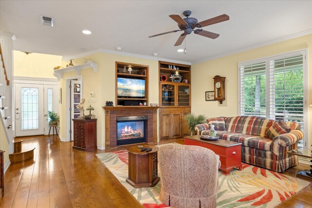 living room with plenty of natural light, a glass covered fireplace, a ceiling fan, hardwood / wood-style floors, and crown molding
