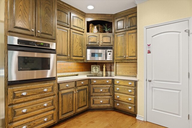 kitchen with stainless steel appliances, light countertops, light wood-style floors, backsplash, and brown cabinetry