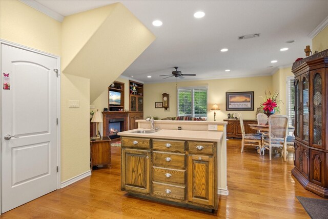 kitchen with a sink, a glass covered fireplace, crown molding, a ceiling fan, and light wood-type flooring