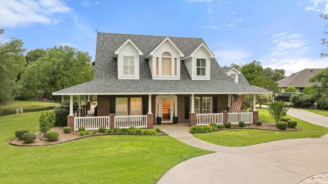 country-style home featuring a porch, roof with shingles, a front yard, and brick siding