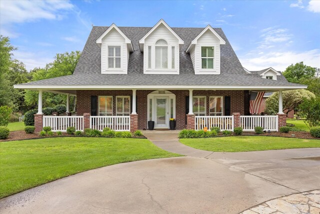 farmhouse-style home with covered porch, brick siding, a front lawn, and roof with shingles