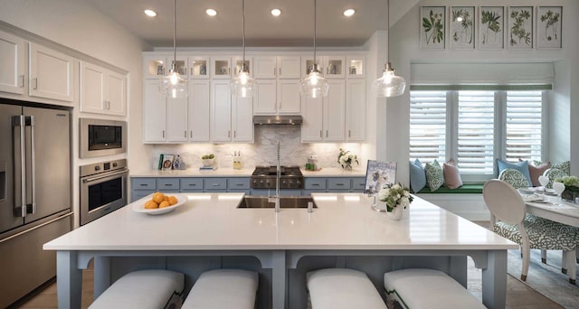 2210 Desmond Dr, Forney, TX 75126 - kitchen with stainless steel appliances, under cabinet range hood, a breakfast bar, white cabinets, and glass insert cabinets
