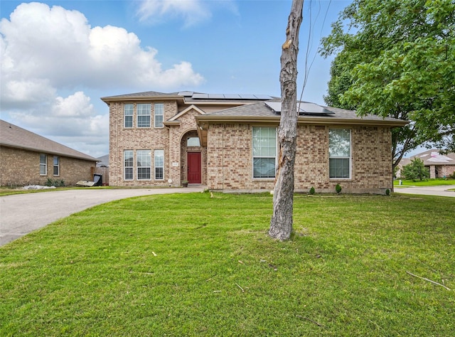view of front of property with a front yard, roof mounted solar panels, and brick siding