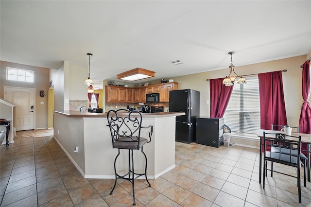 kitchen with black appliances, a peninsula, light tile patterned floors, a breakfast bar, and backsplash