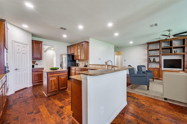 kitchen featuring dark wood-style flooring, light stone countertops, ceiling fan, a kitchen island, and recessed lighting