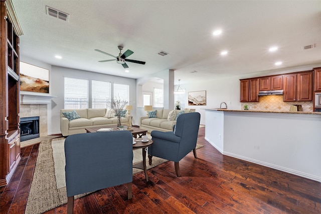 living area featuring a ceiling fan, dark wood finished floors, recessed lighting, a tile fireplace, and arched walkways