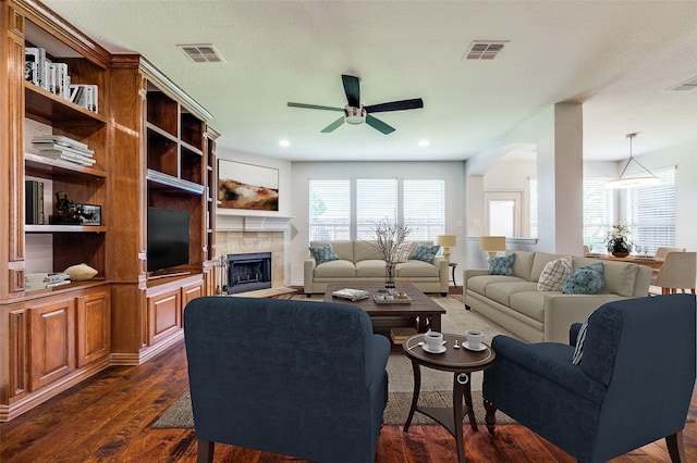 living area featuring ceiling fan, a tile fireplace, dark wood finished floors, arched walkways, and recessed lighting