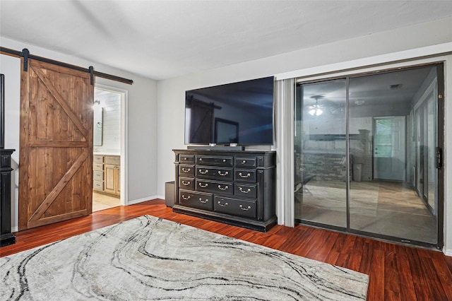 bedroom featuring a barn door, wood finished floors, baseboards, and ensuite bathroom