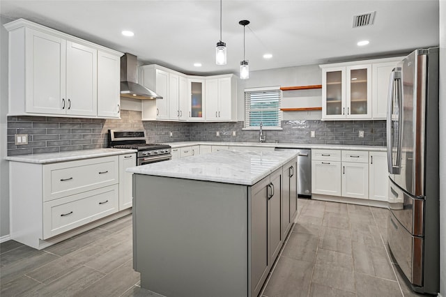 kitchen with stainless steel appliances, wall chimney exhaust hood, decorative backsplash, a kitchen island, and pendant lighting