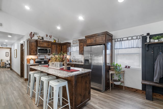 kitchen featuring appliances with stainless steel finishes, a center island, light wood finished floors, a kitchen breakfast bar, and lofted ceiling