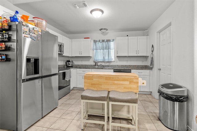 420 Whitney Ct, Rio Vista, TX 76093 - kitchen featuring appliances with stainless steel finishes, light tile patterned floors, white cabinets, dark stone counters, and a breakfast bar area