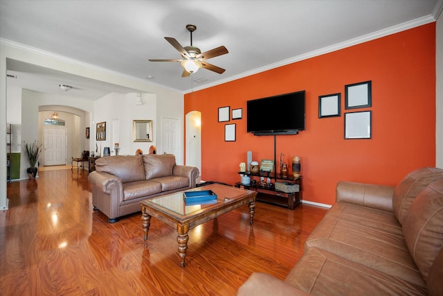 living room featuring arched walkways, ornamental molding, a ceiling fan, wood finished floors, and baseboards