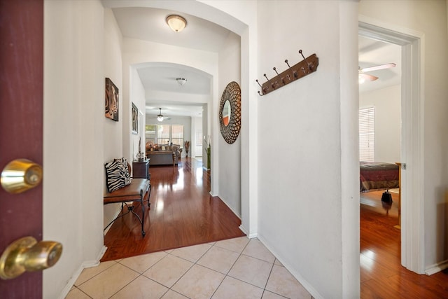 hall featuring arched walkways, light wood-style floors, and baseboards