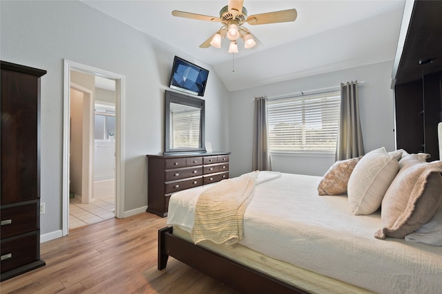 bedroom with vaulted ceiling, light wood-type flooring, ensuite bathroom, baseboards, and a ceiling fan