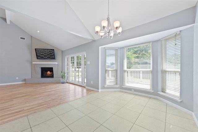unfurnished living room with light tile patterned floors, a chandelier, a brick fireplace, high vaulted ceiling, and baseboards